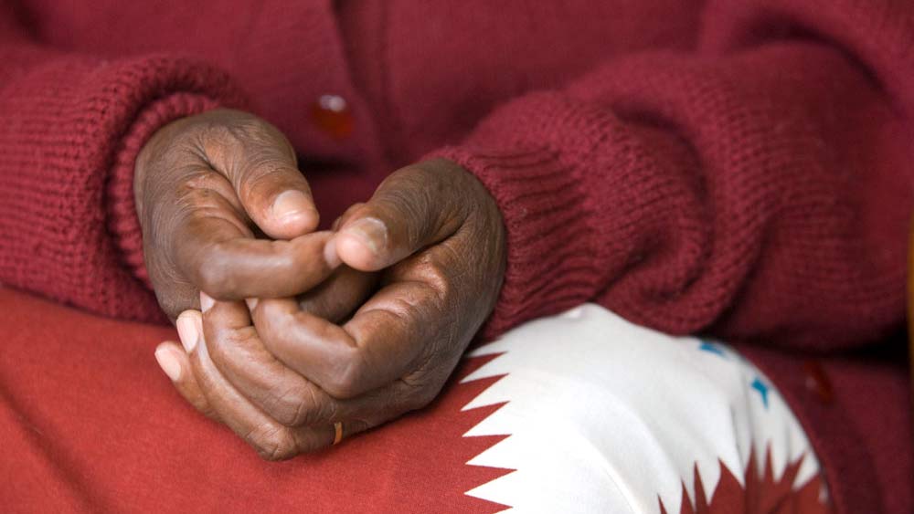 102707_D0187-16x9crop Cropped photo of a woman sitting with hands folded on her lap, wearing maroon sweater and red and white patterned skirt or dress