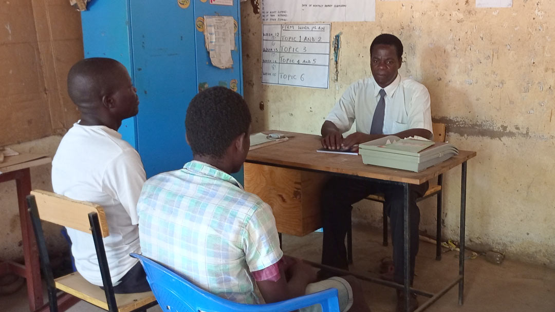 Two young boys sit across the table from their teacher. 