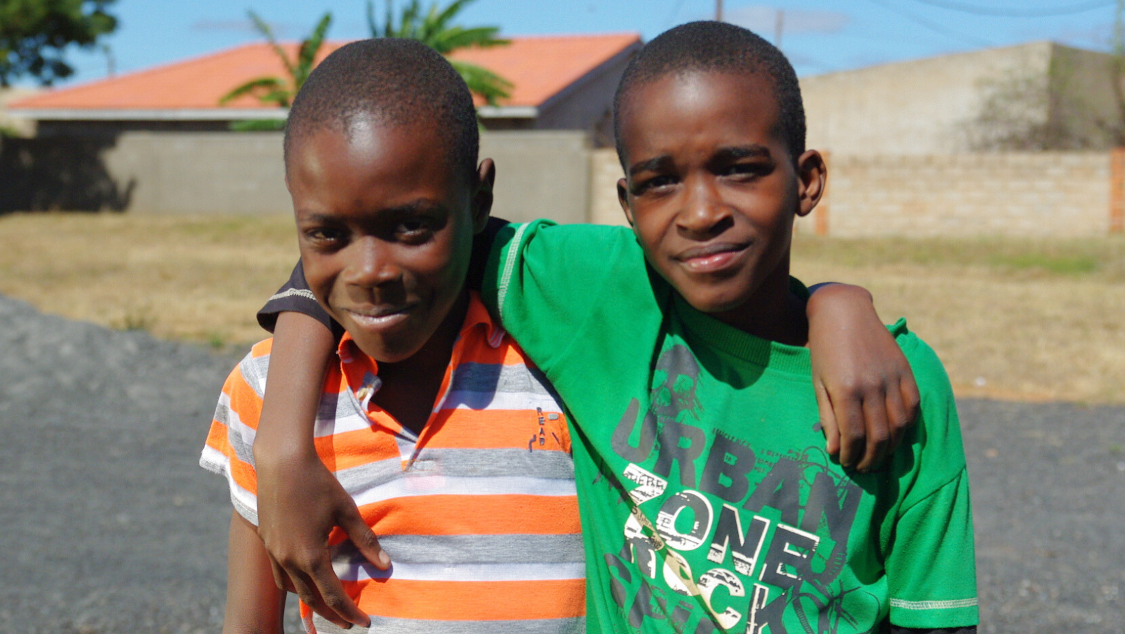 Two boys smile with their arms around each other's shoulders.