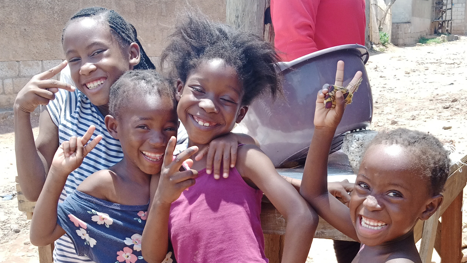 Four girls smile, give the peace sign, and put their arms around each other.